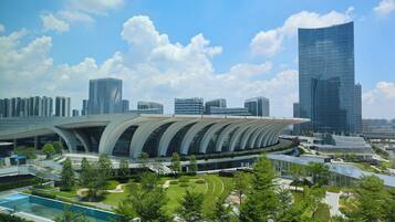 A modern building with a curved roof and a large glass facade, surrounded by greenery and other high-rise buildings in the background.