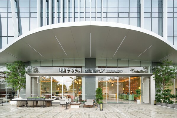 Una entrada de hotel moderna con techo curvo, zona de estar exterior y plantas en macetas.