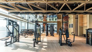 Un gimnasio con equipos de ejercicio variados, ventanas amplias y piso de madera.