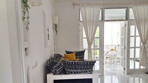 Amplia habitación con un banco blanco, un ventanal con cortinas blancas y vistas al exterior.