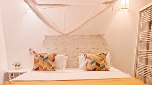 Una cama con cabecera blanca, dos almohadas con estampados geométricos multicolores y una colcha color mostaza.