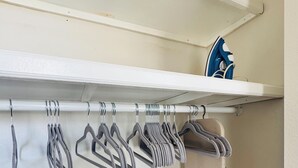 A closet with a white shelf, multiple hangers, and an iron.