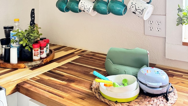 A kitchen with wooden countertops, a hanging pot rack with green mugs, and a variety of kitchen utensils and appliances.