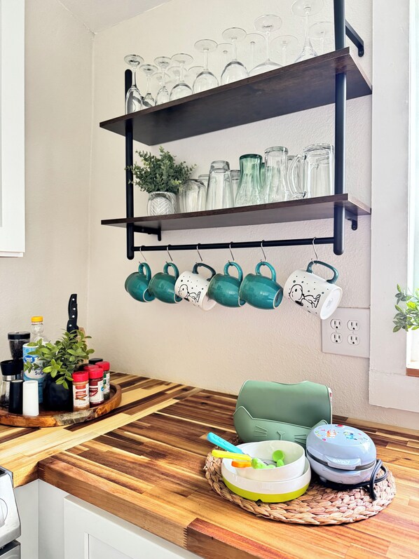 Une cuisine dotée de plans de travail en bois, d’un porte-ustensiles suspendu avec des tasses vertes, et d’une variété d’ustensiles et d’appareils de cuisine.
