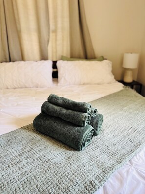 Un lit bien fait, avec des draps blancs et une couverture verte à texture intéressante.