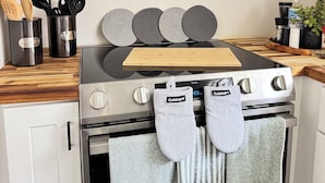 A kitchen with a stainless steel stove, oven, and microwave. There are wooden utensils in a container, a cutting board, and a plant on the counter.