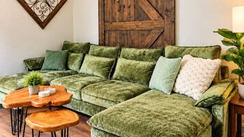 A green sectional sofa with a wooden coffee table and matching ottoman, a decorative wall piece, and a sliding barn door.