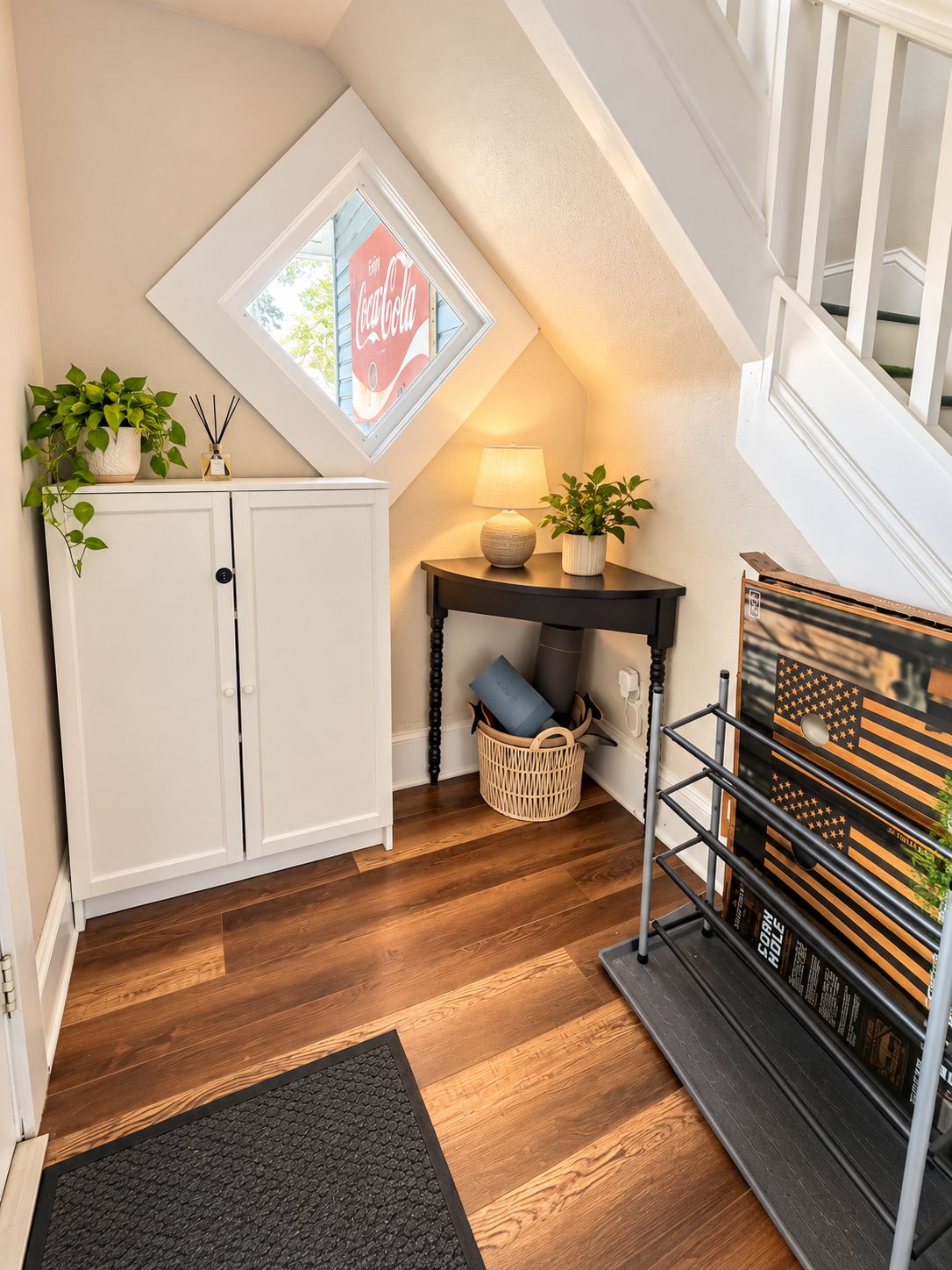 Ein Zimmer mit schrägen Wänden, einem weißen Schrank, einem kleinen Tisch mit Lampe, einem Korbwäscher und einem Bücherregal.