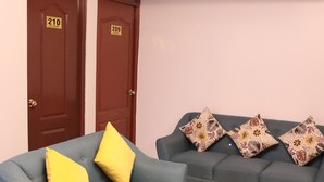Um quarto com duas portas identificadas com os números 210 e 209, uma poltrona azul com almofadas amarelas e um sofá azul com almofadas estampadas.