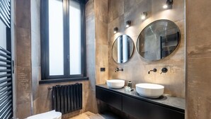 Un baño moderno con dos espejos redondos, un ventanal grande y un tocador negro con dos lavamanos.