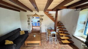 A cozy living area with a sofa, coffee table, and a dining table with chairs. A wooden staircase leads to a kitchen area with blue cabinets and a tiled backsplash. - Charming gîte - 72 m² - 30 min from the sea (Bellevigny)