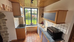 A compact kitchen with a stove, sink, and microwave. It features a window with a view of a garden. - Charming gîte - 72 m² - 30 min from the sea (Bellevigny)