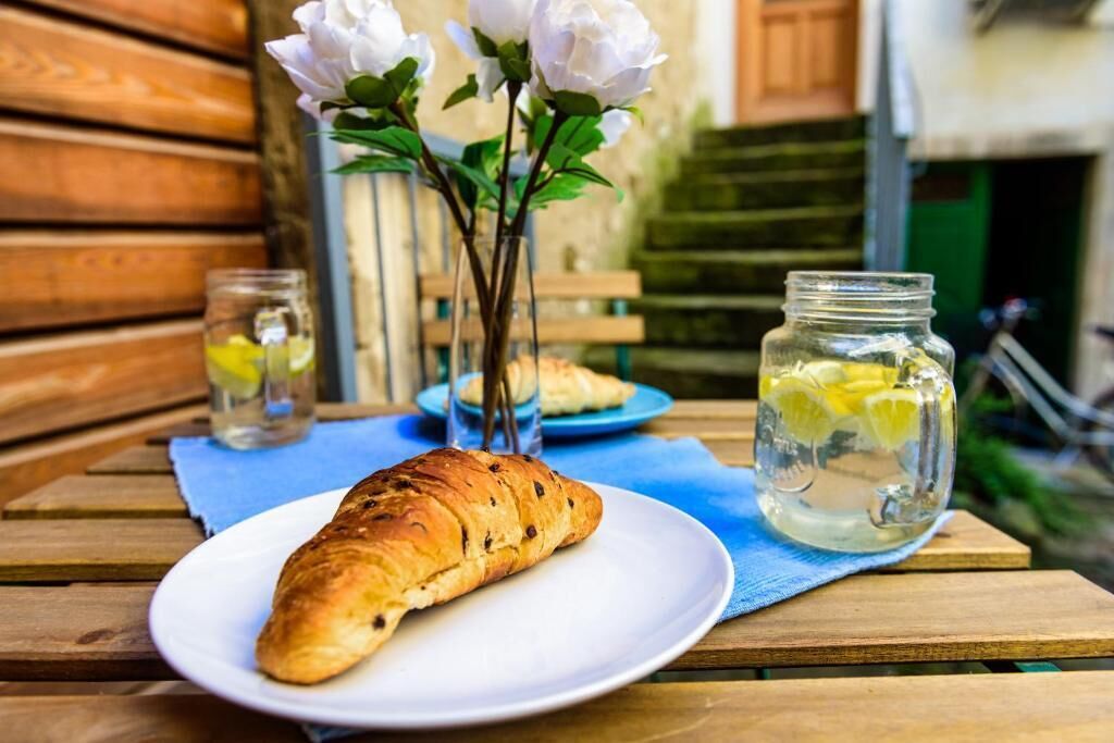Un croissant sur une assiette blanche, un bocal rempli de tranches de citron et un vase avec des fleurs blanches sur une table en bois.