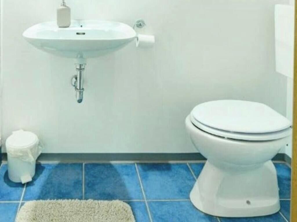 Une salle de bain avec un lavabo blanc, des toilettes et un sol carrelé de bleu.