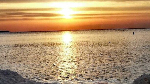 Ein Sonnenuntergang über einem ruhigen Meer mit einer fernen Küstenlinie.