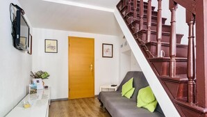 Ein Zimmer mit einer Holztreppe, einem grauen Sofa mit grünen Kissen, einer Holztür und einem kleinen weißen Tisch mit einer Pflanze.