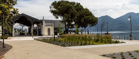 Un sendero pavimentado que lleva a una estructura cubierta, con vista a un lago y montañas.