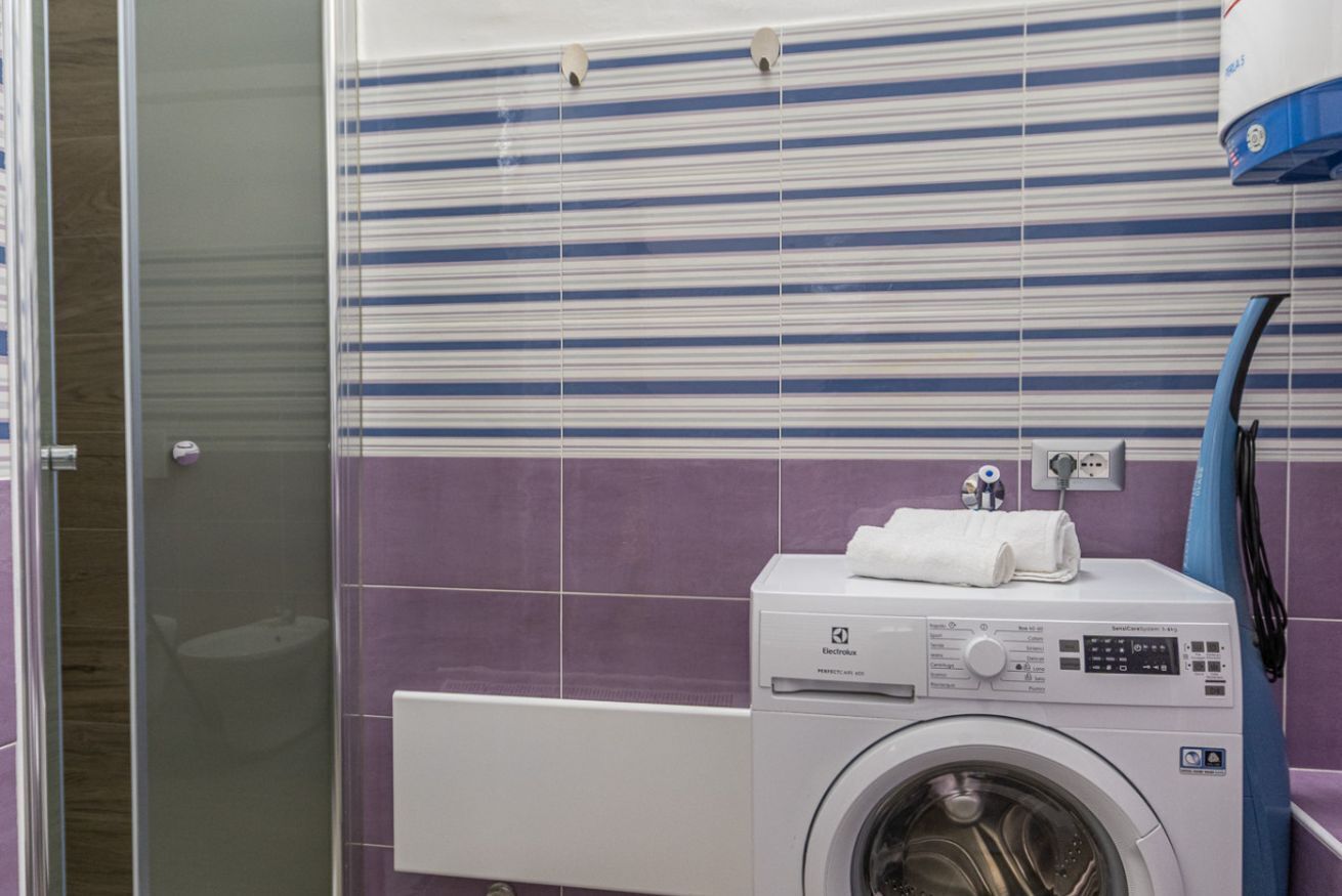 A compact laundry area with a washing machine, a drying rack, and a glass shower enclosure.