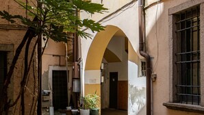 Un vicolo con un edificio caratterizzato da un portale ad arco, una pianta in vaso e una finestra con inferriate.