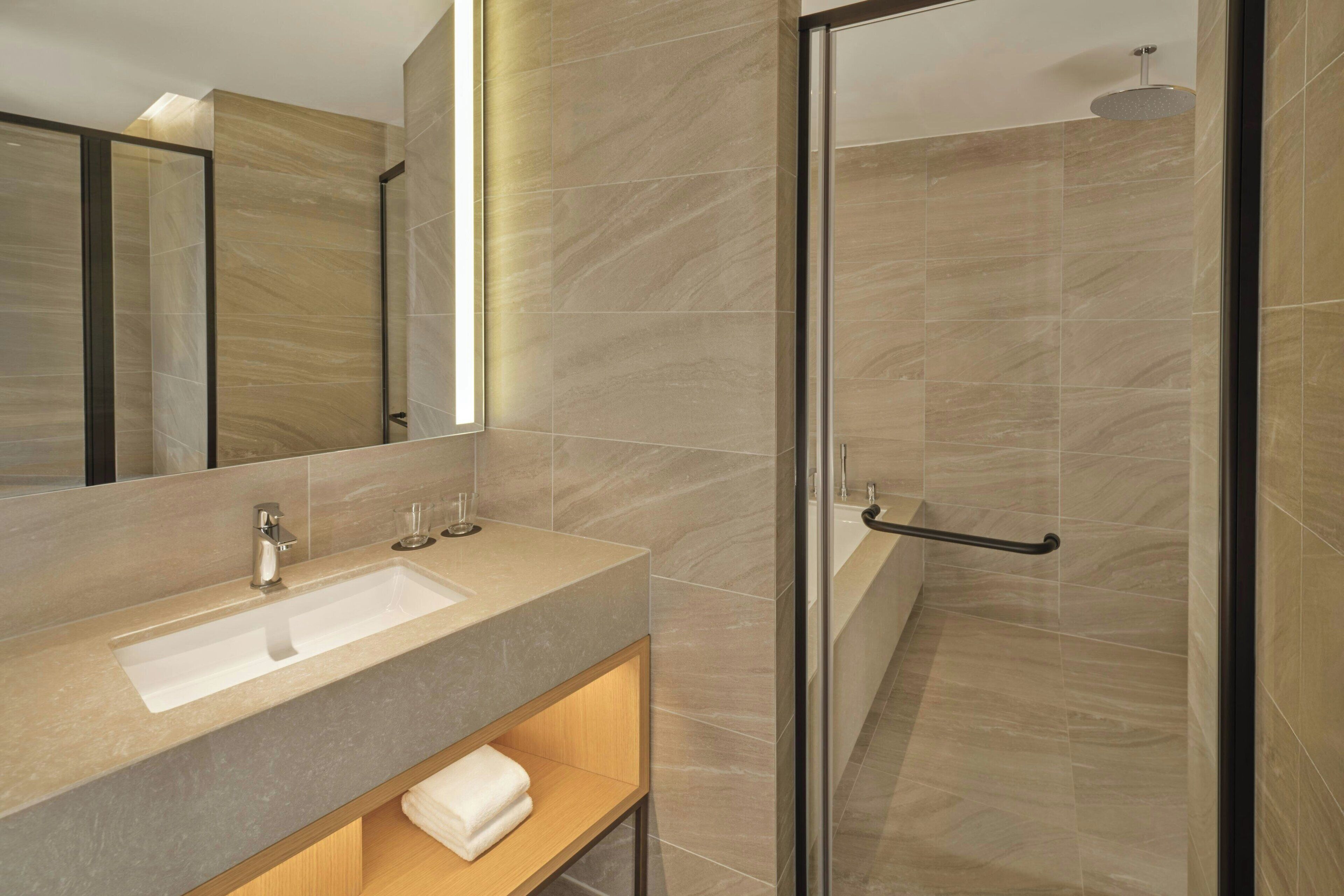 A modern bathroom with a large mirror, a sink, and a shower area.