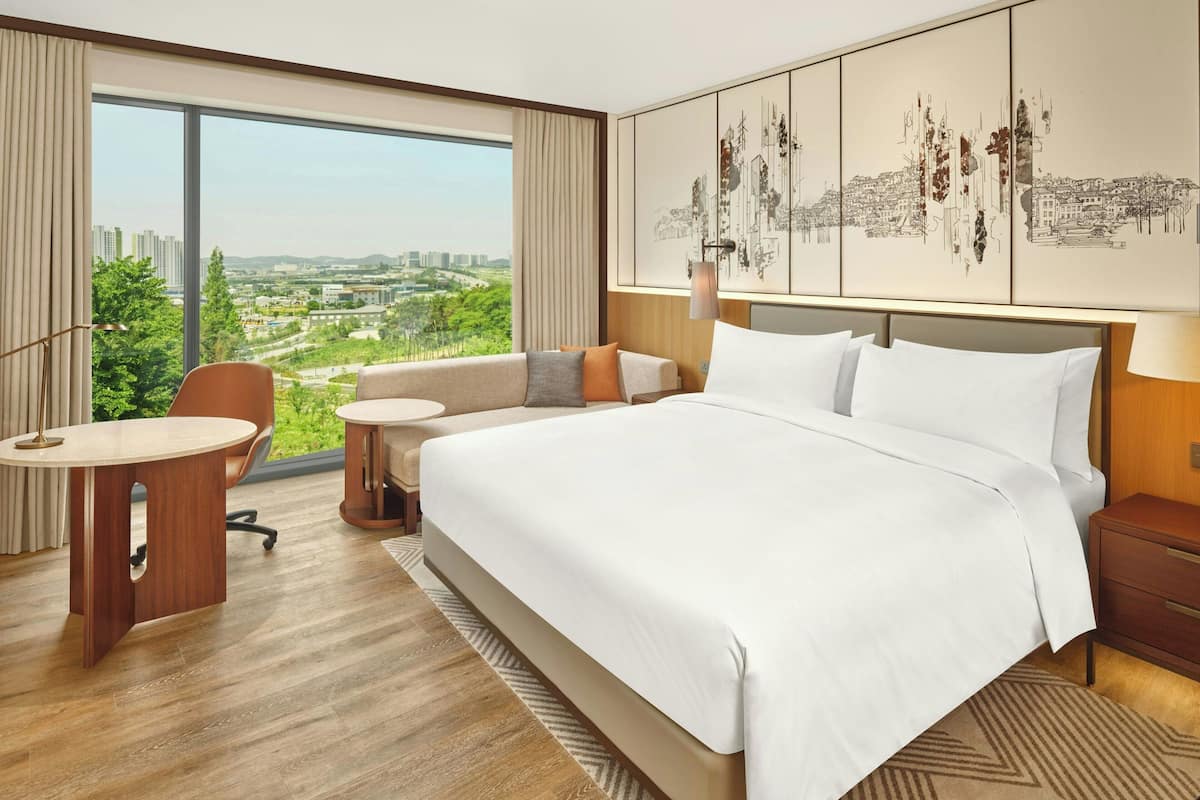 Habitación de hotel con una cama grande, un sofá, un escritorio y vistas a un paisaje urbano.