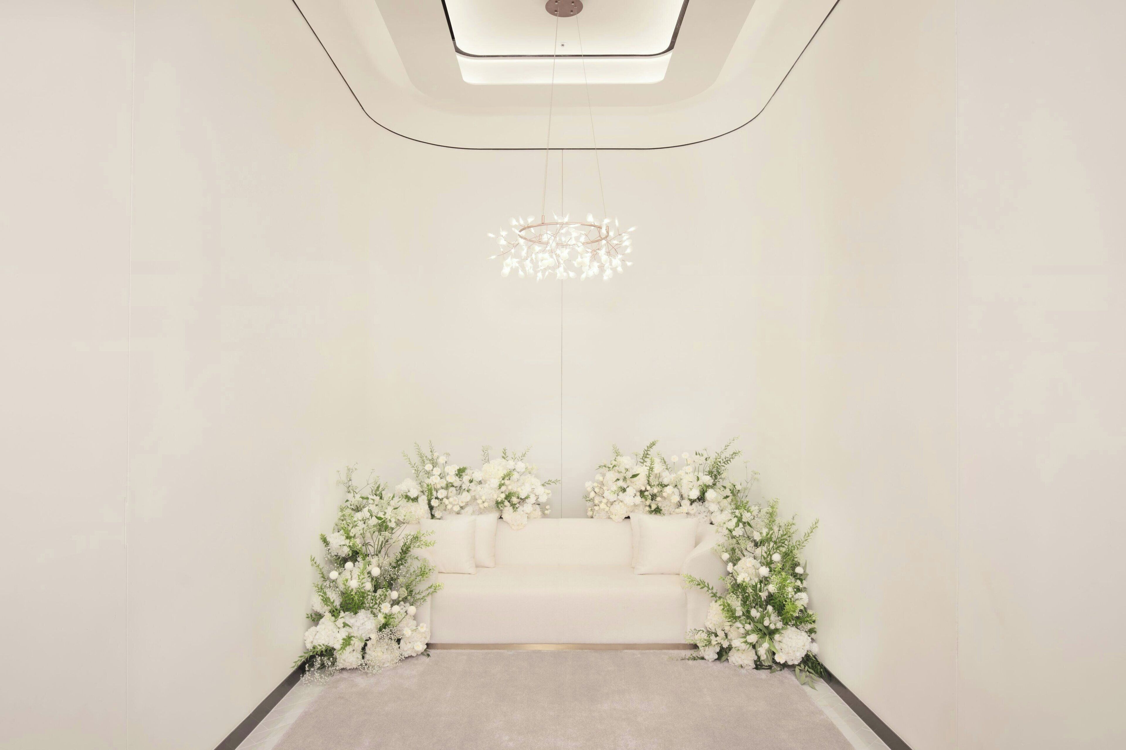 A minimalist room with a white sofa, floral arrangements, and a modern chandelier.