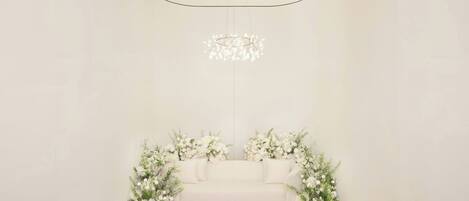 A minimalist room with a white sofa, floral arrangements, and a modern chandelier.