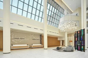 Eine geräumige Lobby mit hoher Decke, großen Fenstern und einem zentralen Kronleuchter.