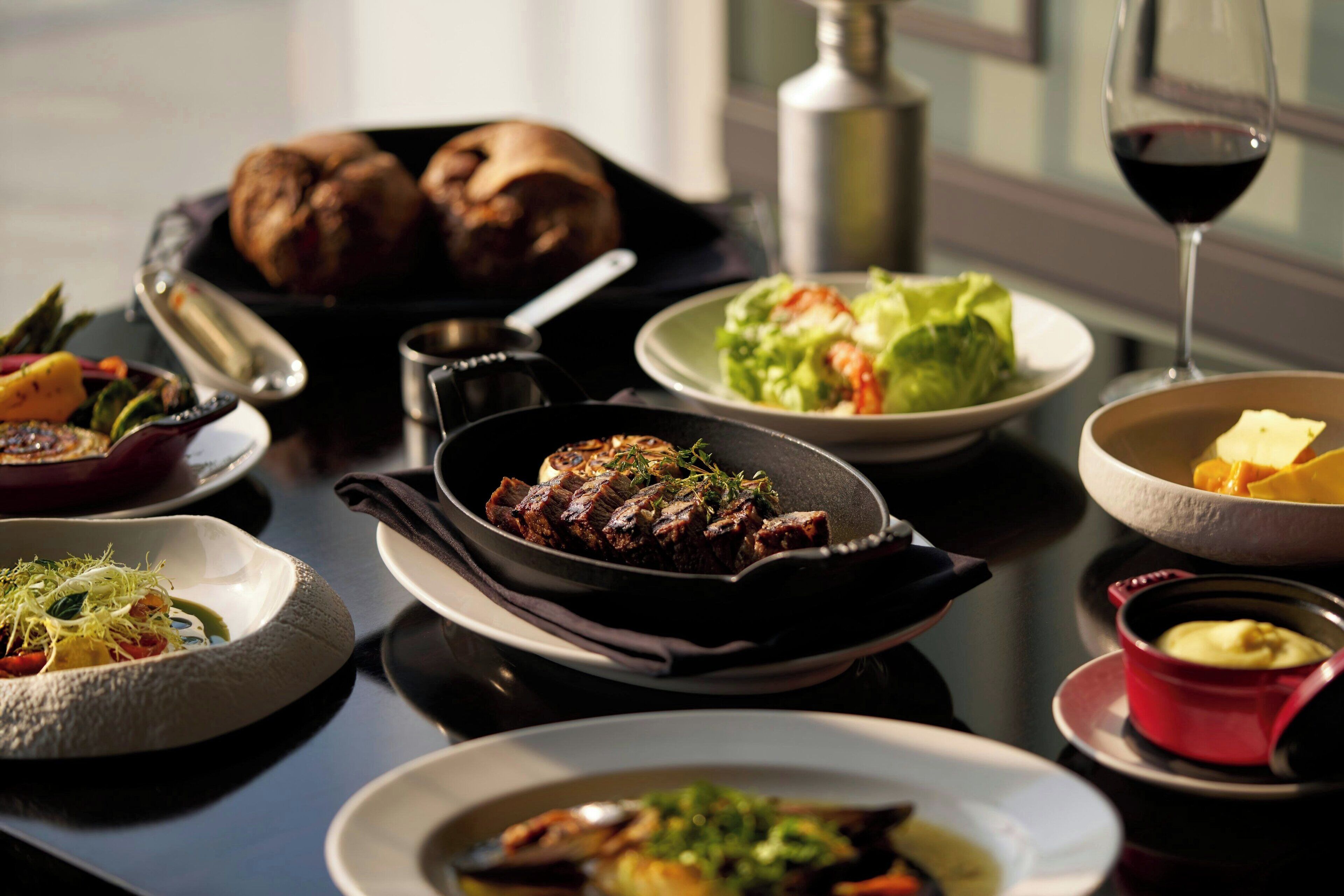 A dining table with various dishes, including a steak, vegetables, and bread.
