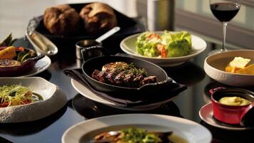 A dining table with various dishes, including a steak, vegetables, and bread.