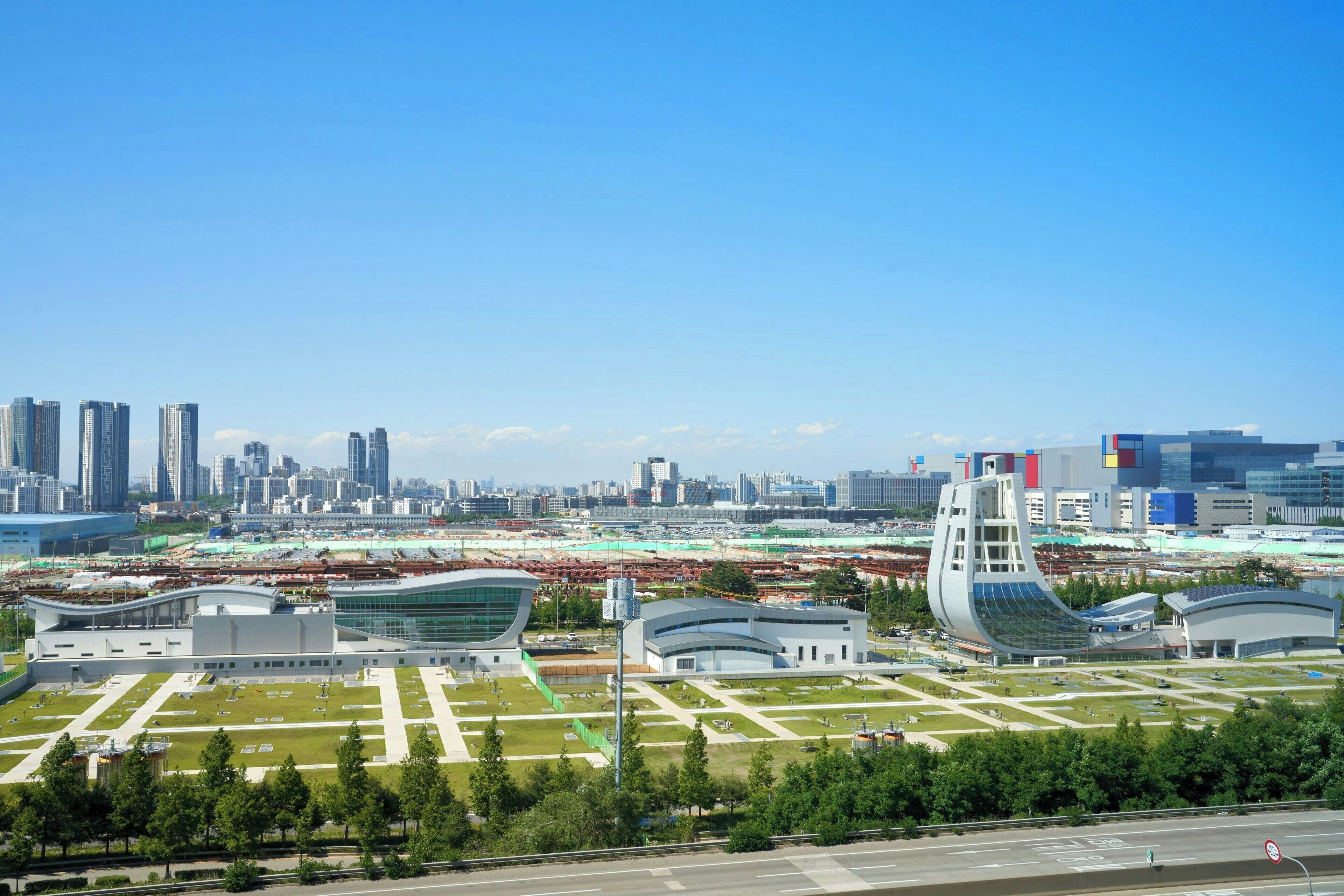Un paysage urbain moderne, caractérisé par une architecture originale, notamment un bâtiment aux lignes courbes et un grand stade.