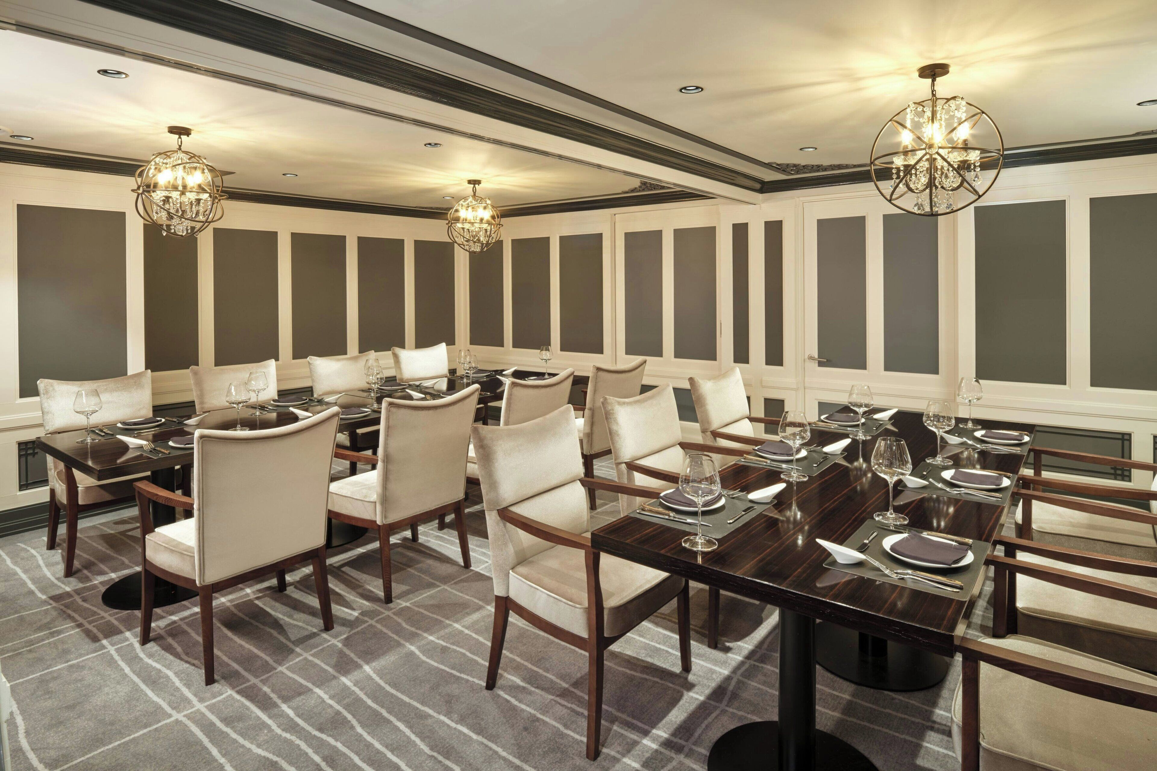 A formal dining room with multiple tables and chairs, elegant chandeliers, and a checkered carpet.