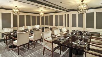 A formal dining room with multiple tables and chairs, elegant chandeliers, and a checkered carpet.