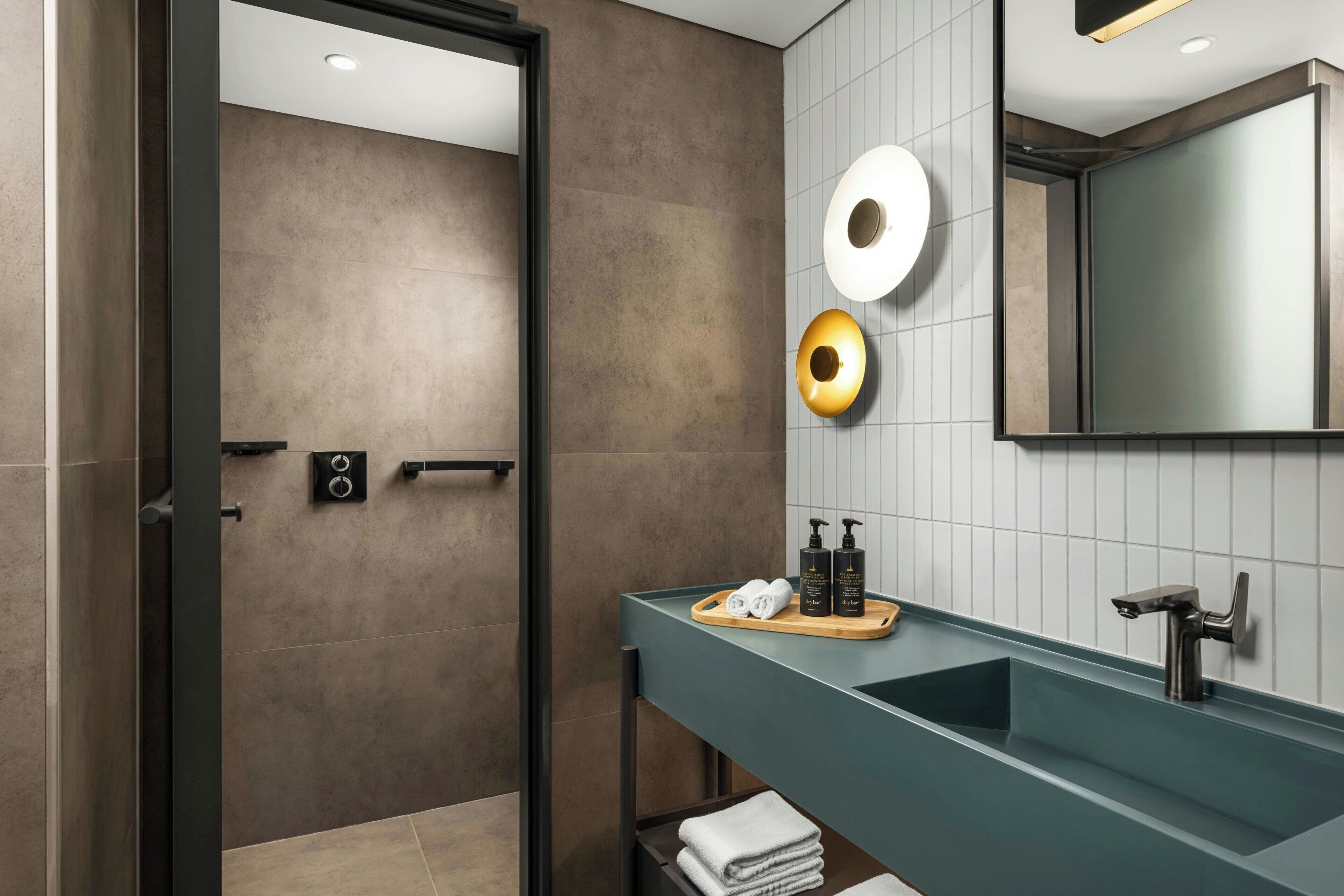 A modern bathroom with a dark-toned shower, a vanity with a teal countertop, and two round mirrors.