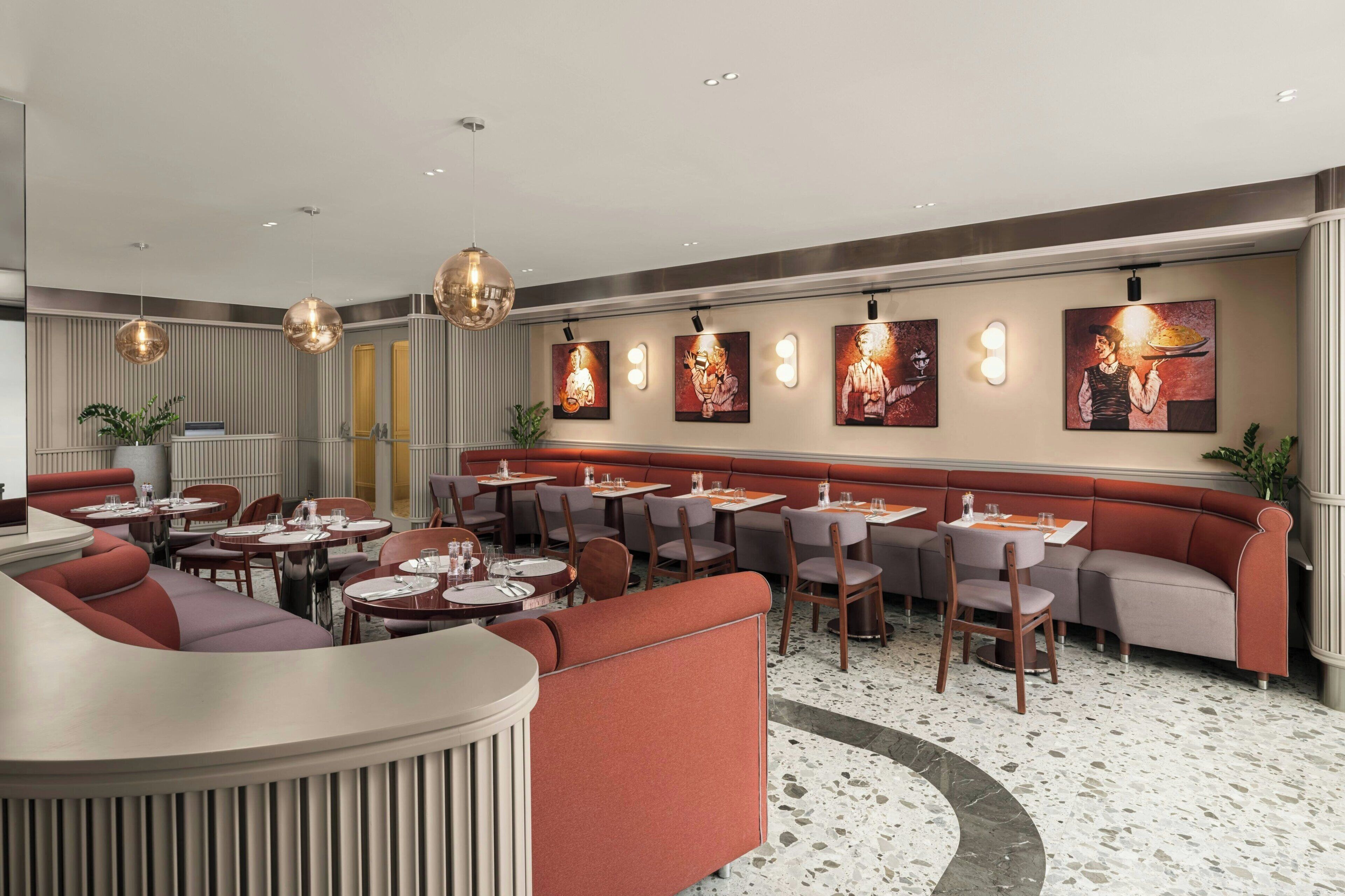 A restaurant interior with round tables, red seating, and artwork on the walls.