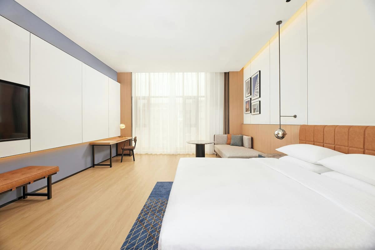 Ein Hotelzimmer mit einem großen Bett, einem Schreibtisch, einem Sessel, einer Couch und einem Fernseher.