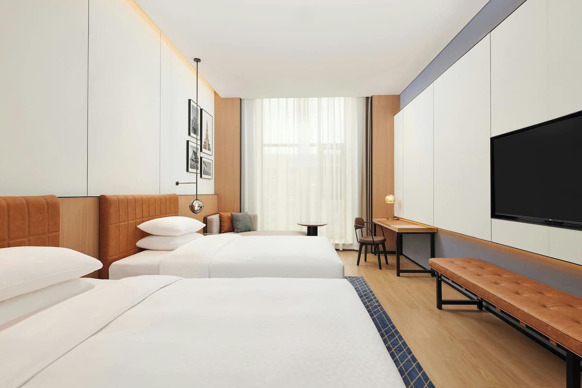 Ein Hotelzimmer mit zwei Betten, einem Schreibtisch, einer Bank und einem Fernseher.