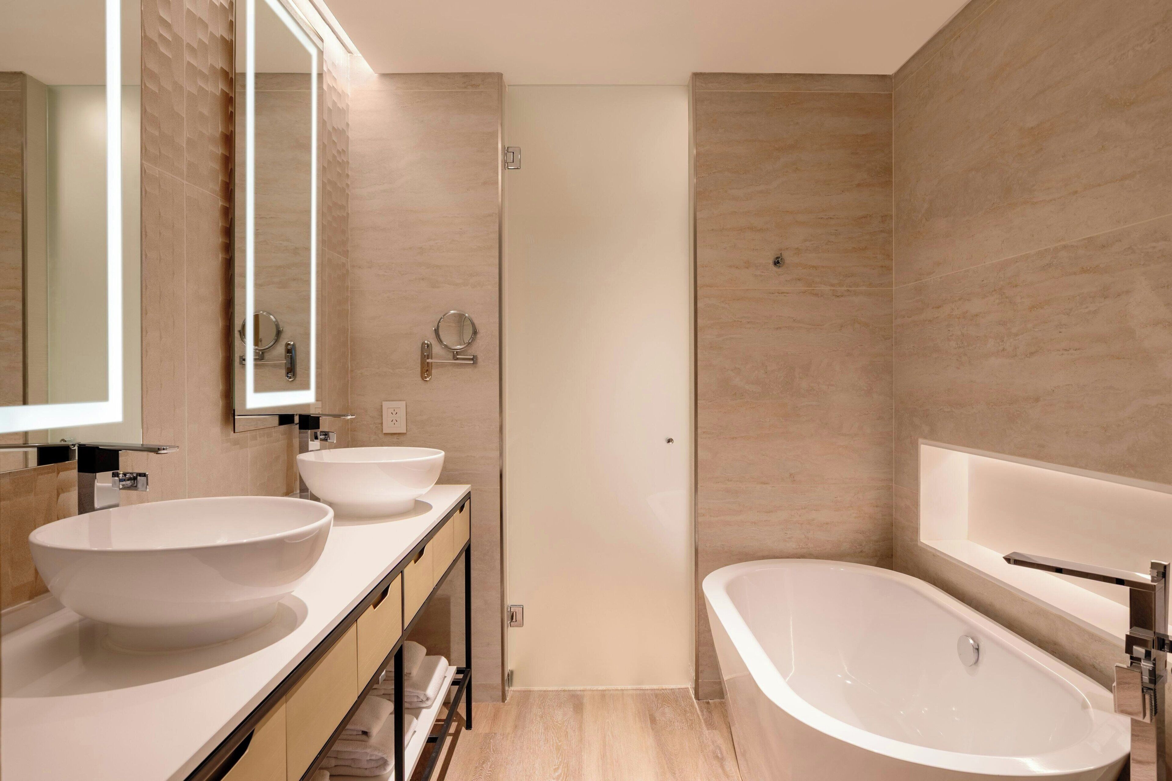 A modern bathroom with two sinks, a bathtub, and a large mirror.