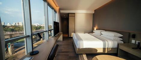 Una habitación de hotel moderna con una cama grande, un escritorio y vistas a la ciudad a través de amplios ventanales.