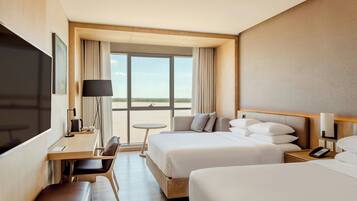 Habitación de hotel con una cama grande, una cama más pequeña, un escritorio con silla, un televisor y vistas al exterior.