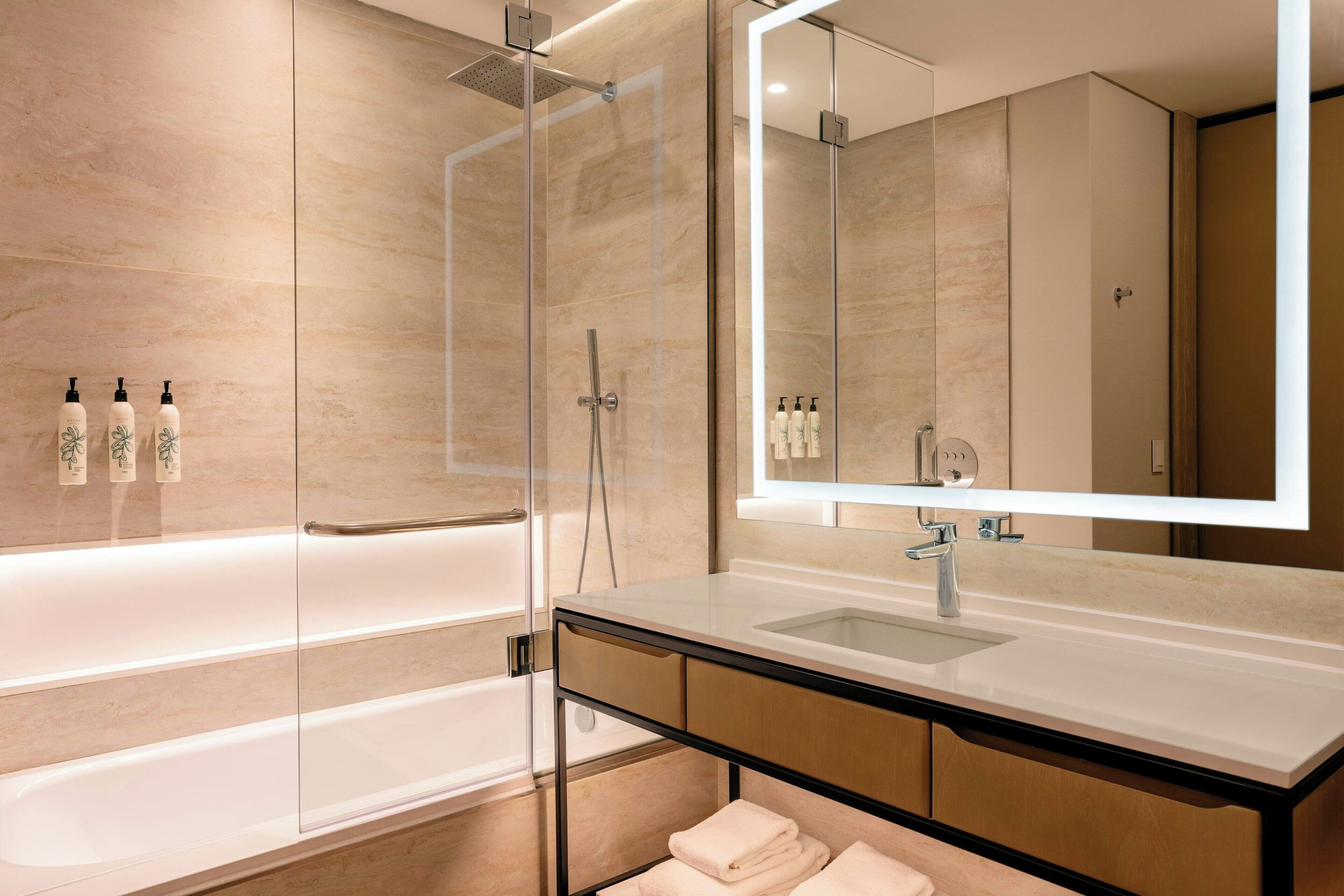Un baño moderno con cabina de ducha acristalada, un espejo grande y un lavabo blanco.