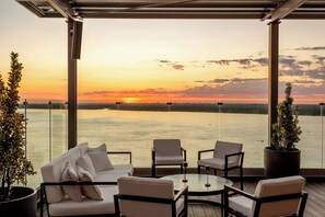A terrace with a view of a sunset over a body of water, furnished with a sofa, chairs, and a small table. - Marriott Corrientes Hotel (Corrientes)