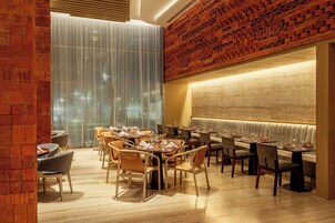 Interior de restaurante con pared de ladrillo, un ventanal con cortinas traslúcidas y una zona de estar con un largo banco.