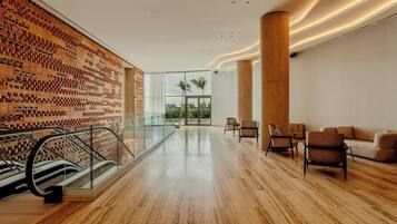 A spacious lobby with a wooden floor, a patterned wall, a glass railing, and a seating area with chairs and a sofa.