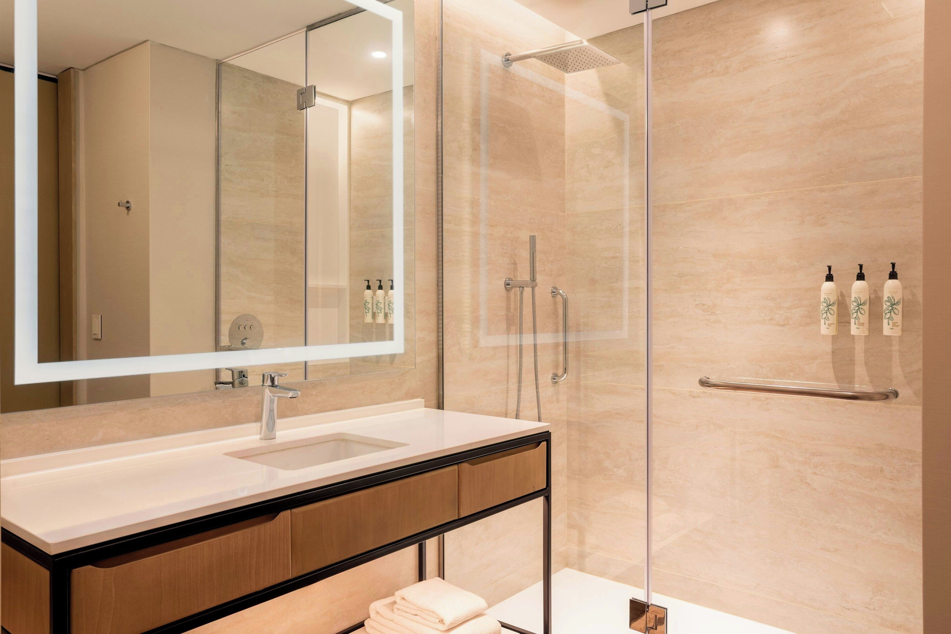 A modern bathroom with a glass-enclosed shower, a large mirror, and a vanity with a sink.