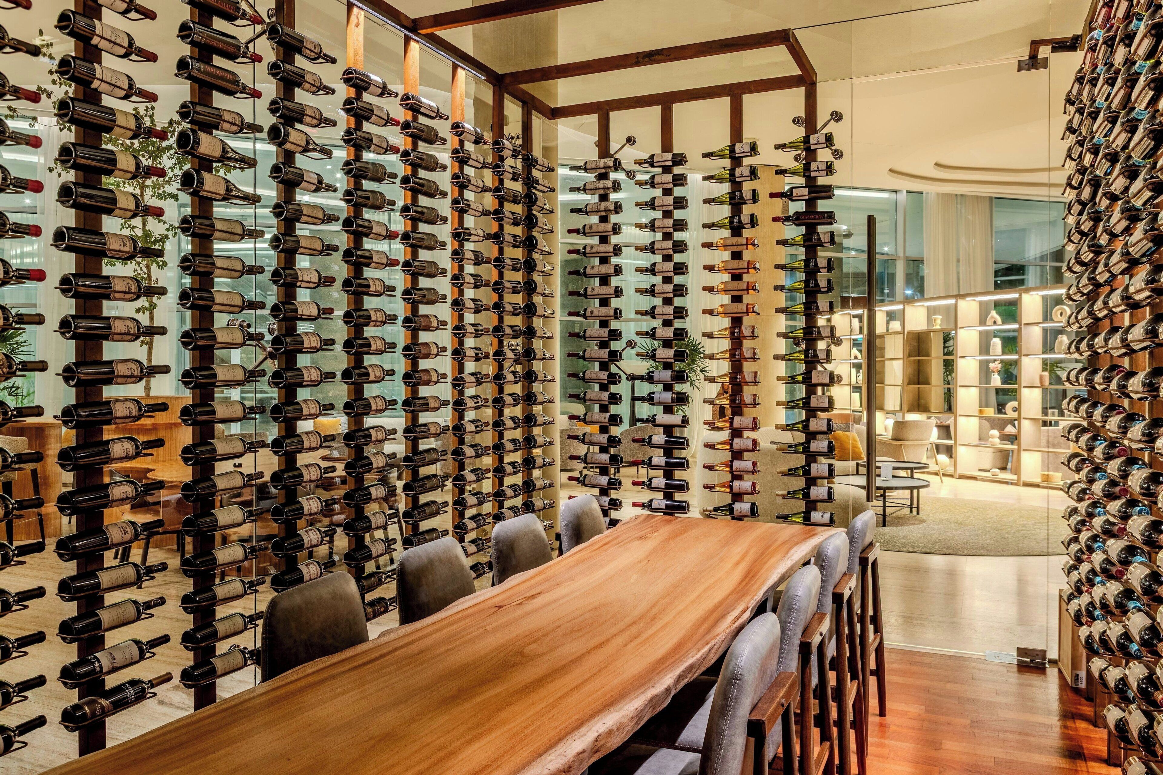 Una habitación con una larga mesa de madera y sillas, rodeada de paredes con filas de botellas de vino.