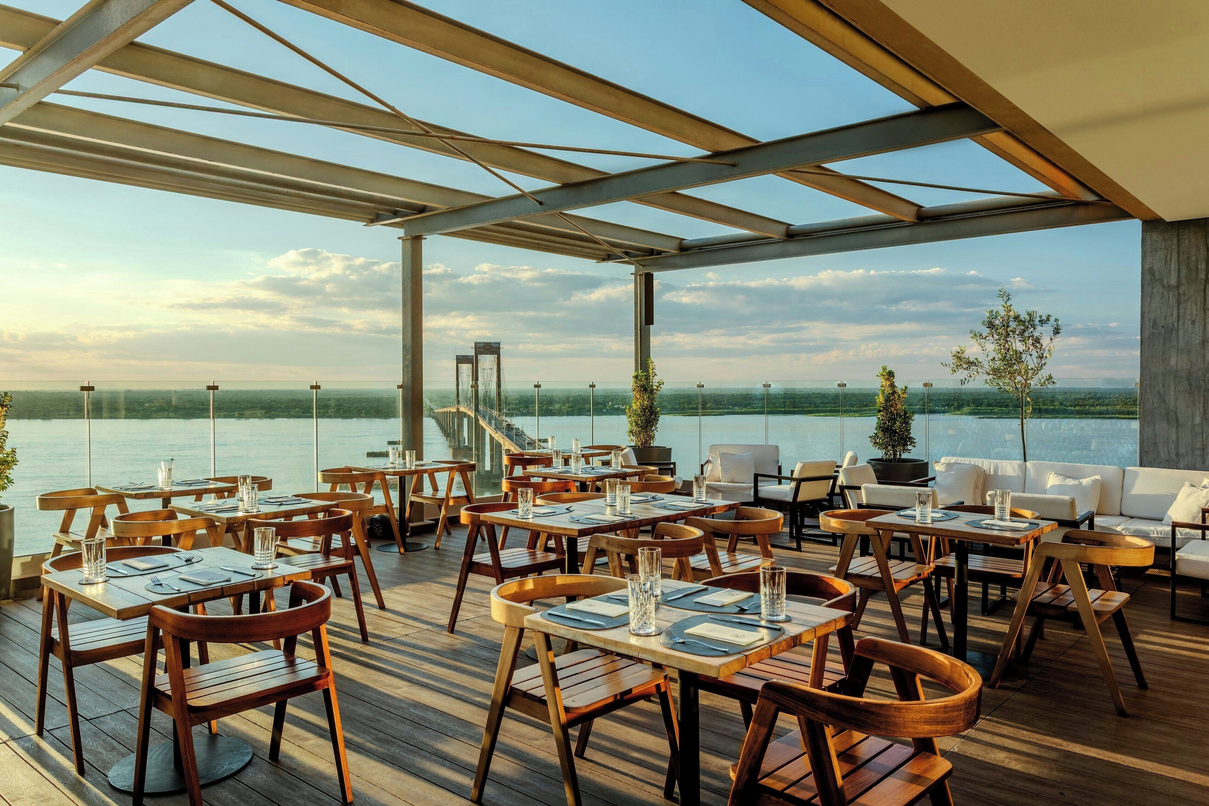 An outdoor dining area with tables and chairs, overlooking a body of water.