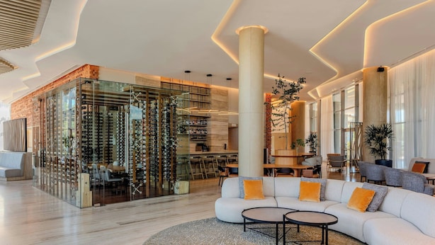 A modern interior with a glass wine rack, a seating area with a sofa and coffee table, and a bar with stools. - Marriott Corrientes Hotel (Corrientes)