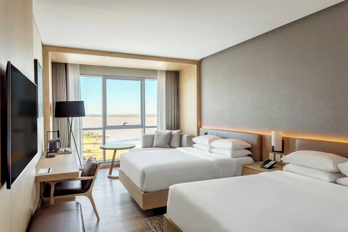 Ein Hotelzimmer mit zwei Betten, einem Schreibtisch, einem Fernseher und einem großen Fenster mit Blick.