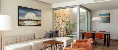 A modern living room with a sofa, coffee table, and leather chairs, a dining area with a table and chairs, and artwork on the walls.
